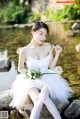 A woman in a white dress sitting on a rock by a river.