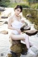 A woman in a white bathing suit sitting on a rock in the water.