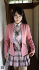 A woman in a pink blazer and plaid skirt posing for a picture.