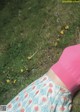 A woman laying on the grass in a pink sweater and floral skirt.