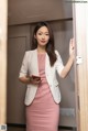 A woman in a pink dress and white blazer holding a cell phone.