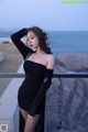 A woman in a black dress posing by the ocean.