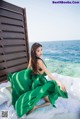 A woman in a green dress sitting on a bed by the ocean.