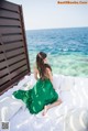 A woman in a green dress sitting on a bed by the ocean.