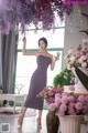 A woman in a purple dress standing in front of a bunch of flowers.