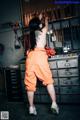 A woman in an orange jumpsuit standing in front of a wall of tools.