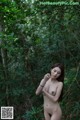 A naked woman standing in the middle of a forest.