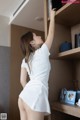 A woman in a white dress leaning against a bookshelf.