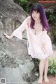 A woman in a pink dress leaning against a rock.