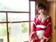 A woman in a red and white kimono standing by a window.