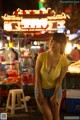 A woman in a yellow shirt and blue shorts standing in front of a market.