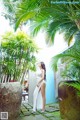 A woman in a white dress standing in front of a palm tree.