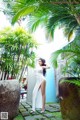 A woman in a white dress standing in front of a palm tree.