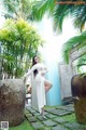 A woman in a white dress standing next to a large stone pillar.